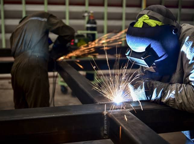 A welder joining a steel frame as sparks fly